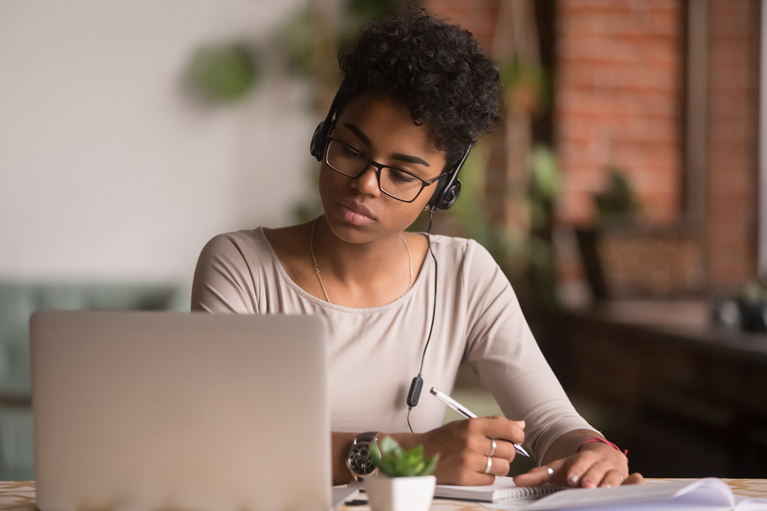 Woman sitting at desk in front of laptop taking notes with headphones on