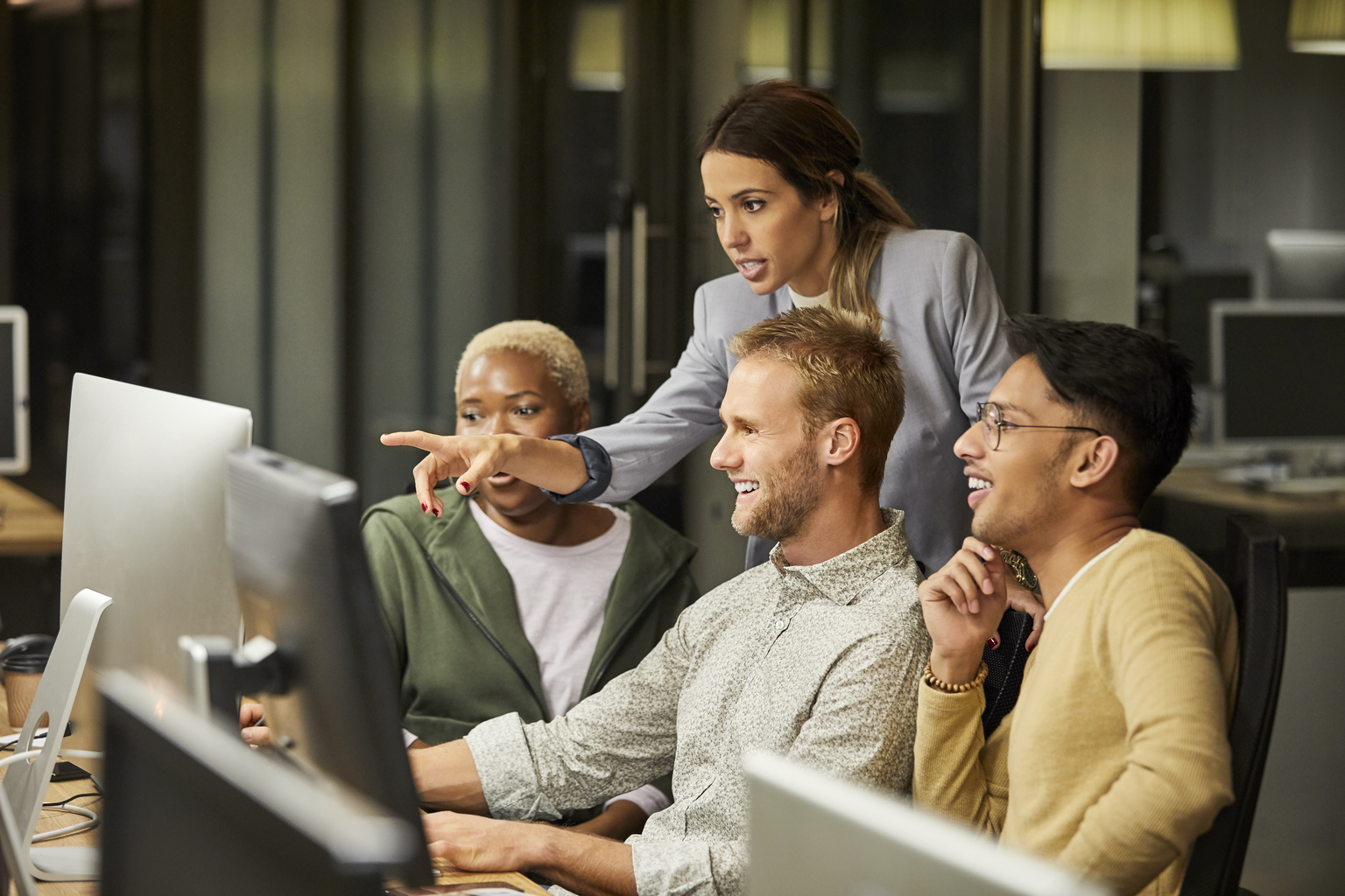 Businesswoman pointing while discussing with coworkers over computer monitor. Multi-ethnic business professionals are planning at workplace. They are in creative office.