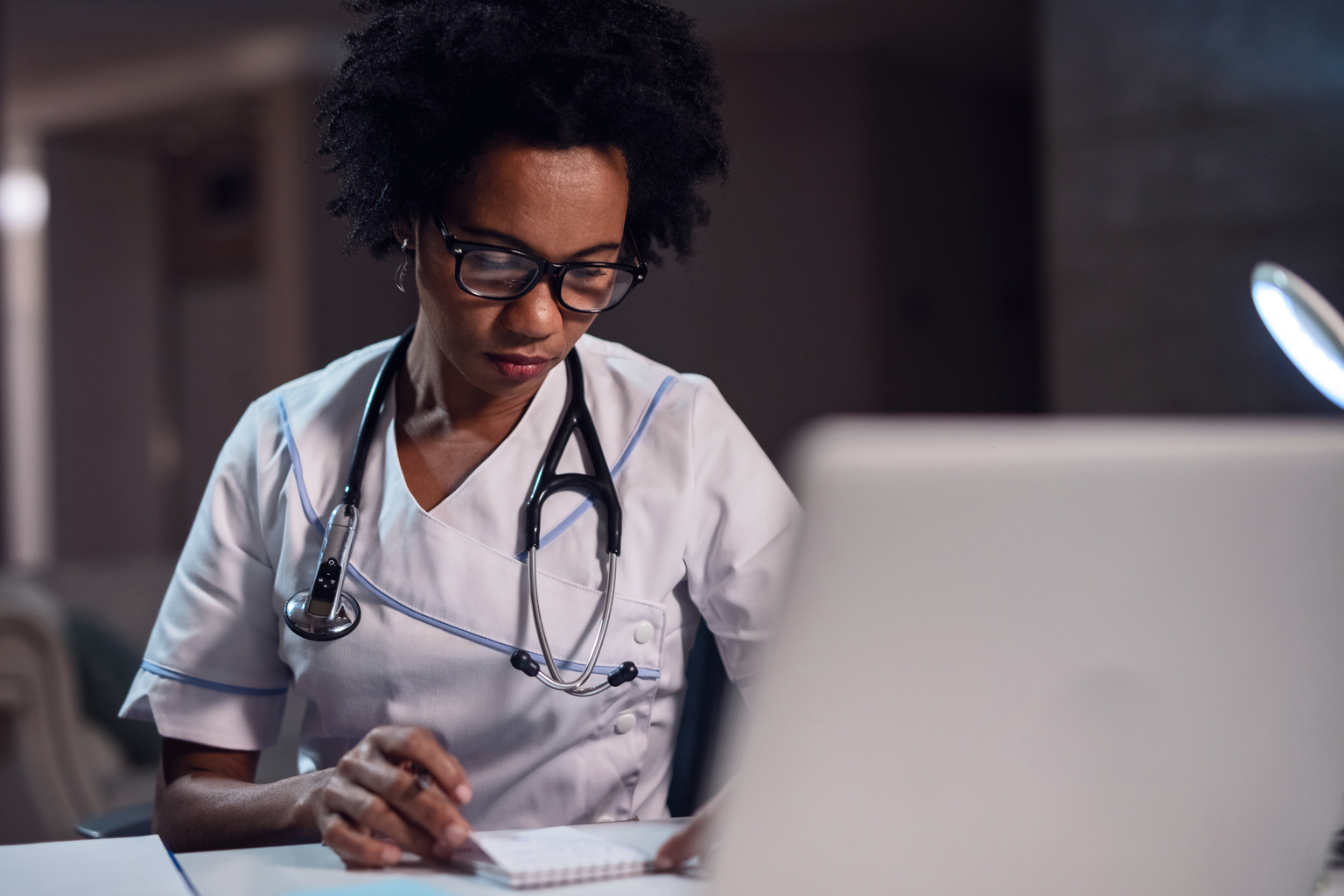 African American female doctor reading notes at office desk