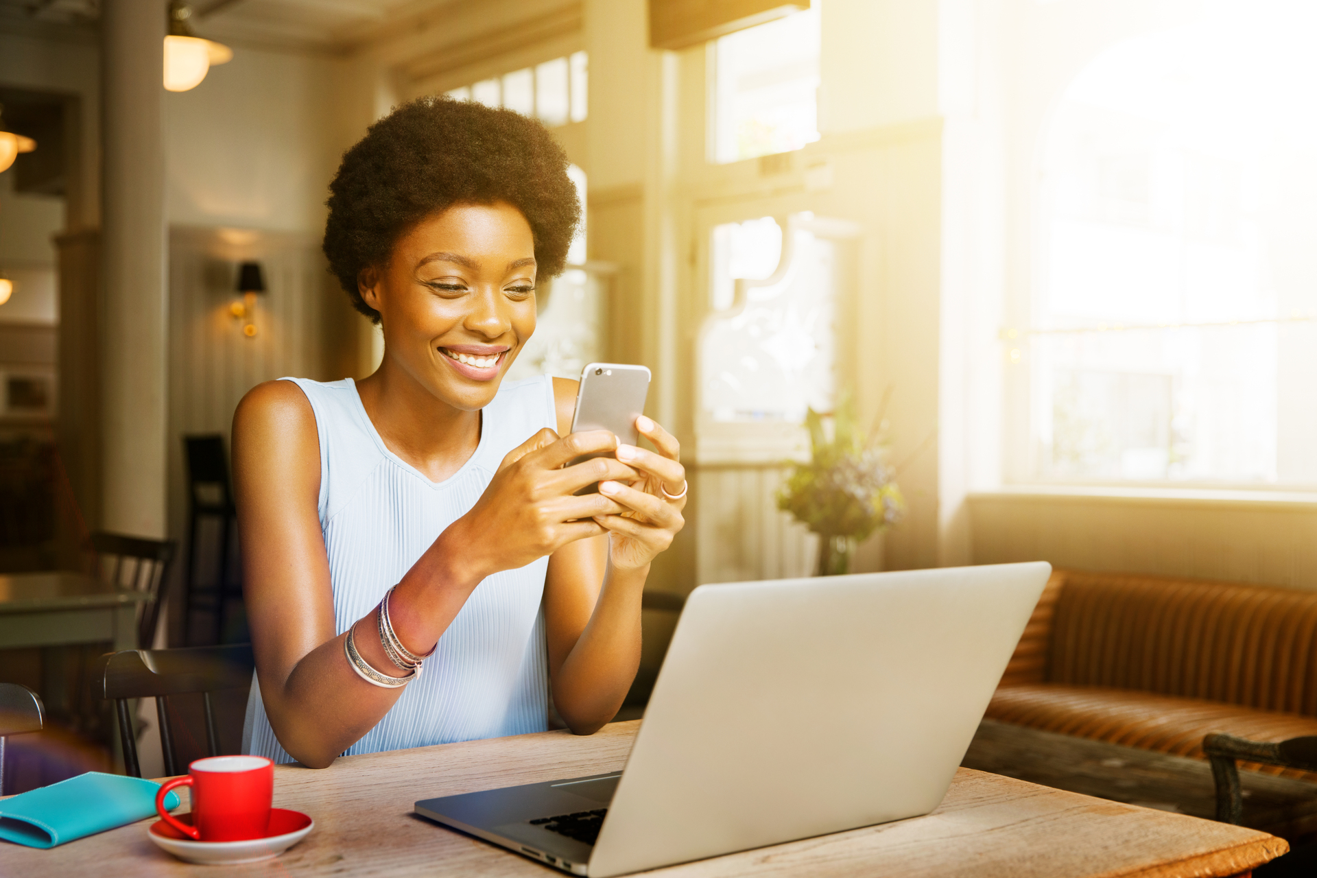 Woman with blue shirt, sitting down with red coffee mug and smiling at her silver phone, Q3 2021, TAA NA US - Preparer