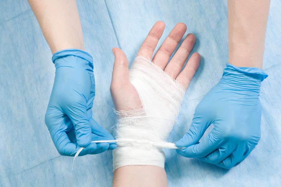 Glove hands tying off the gauze on a gauzed-wrapped hand