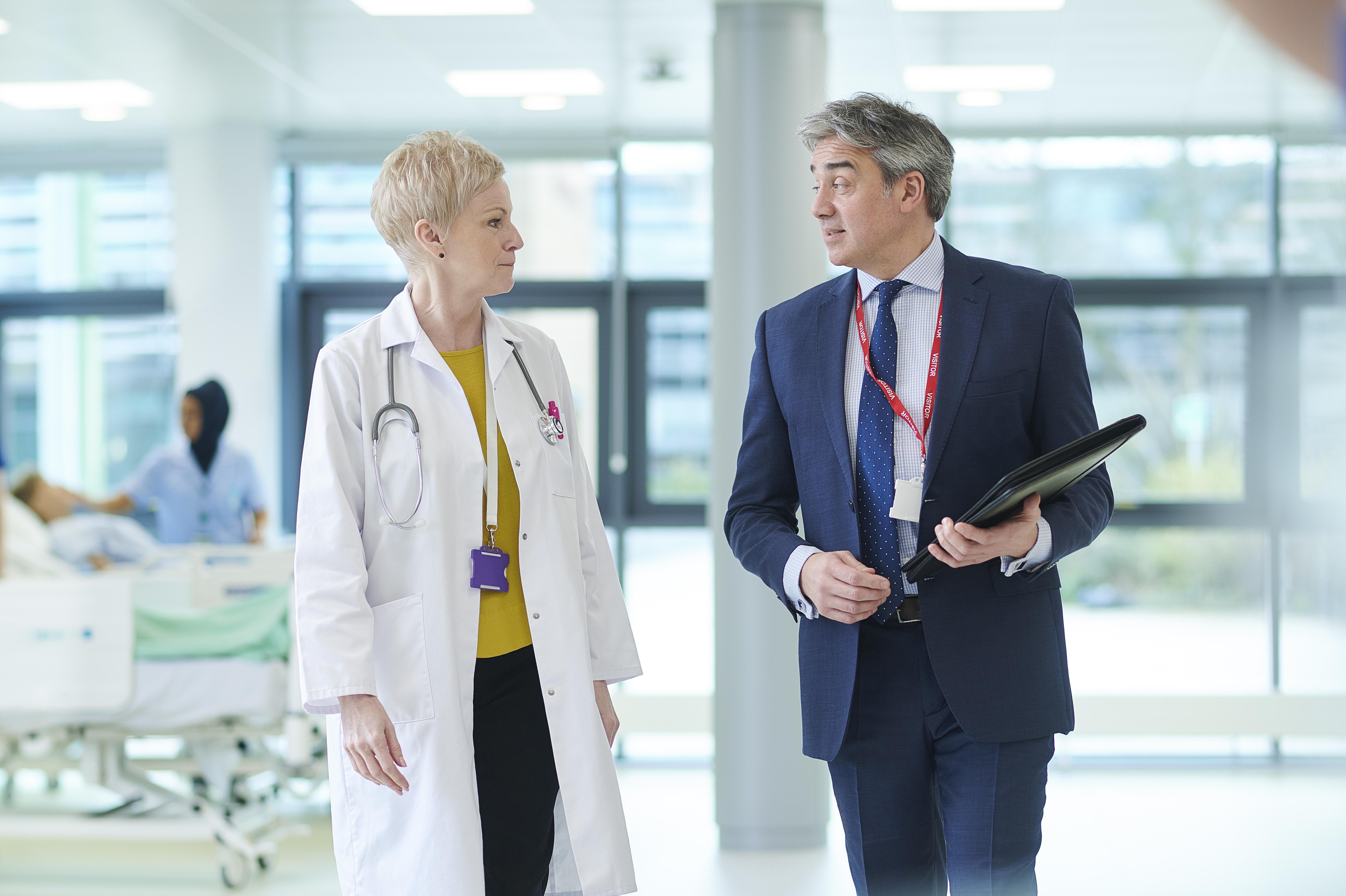 a women doctor with short blonde hair talking with a business man with navy suit in hospital