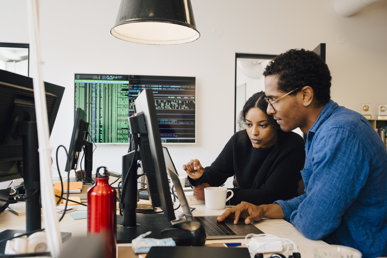 Focused male and female engineers coding over laptop on desk in office