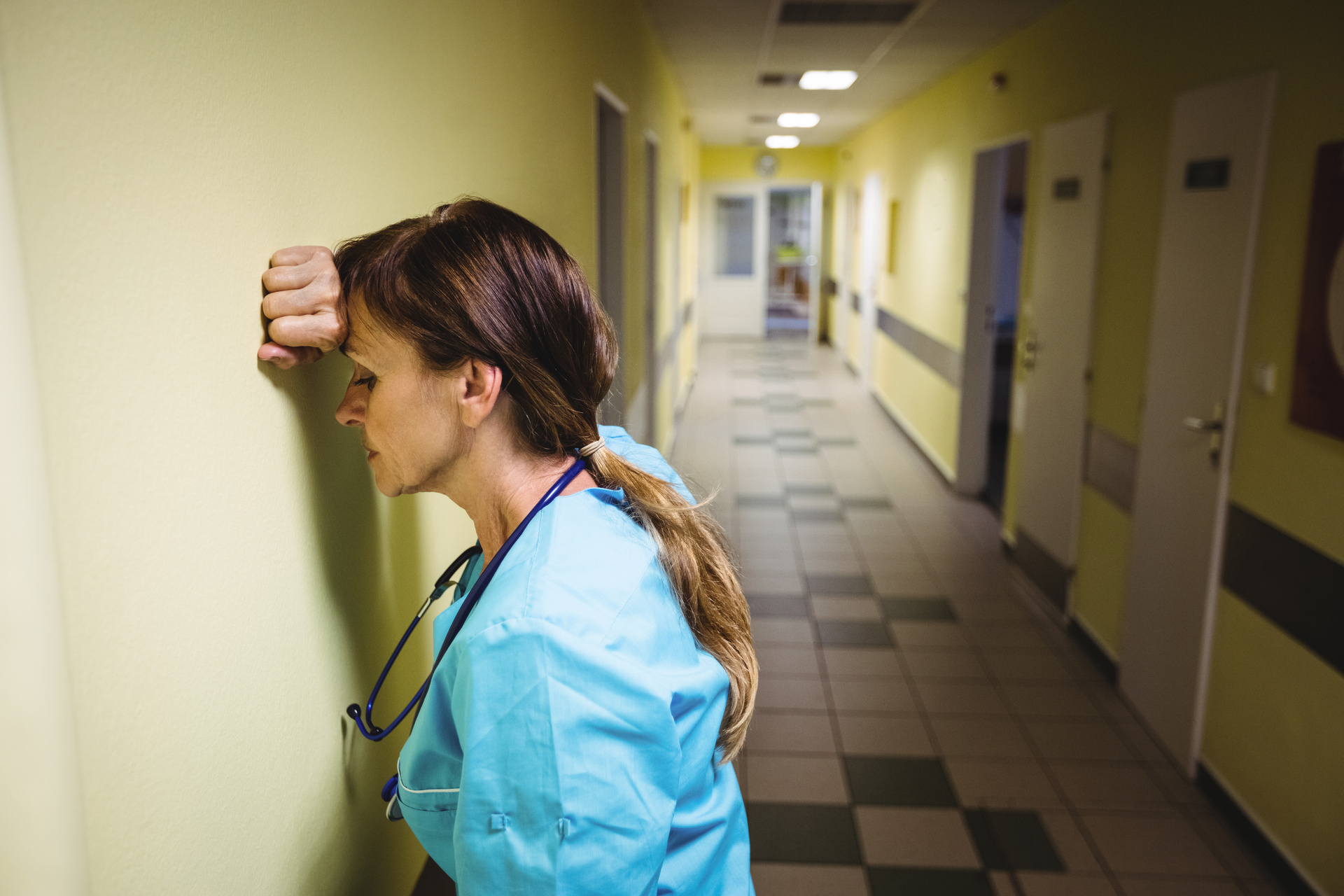 Frustrated nurse leaning against wall of hospital wing