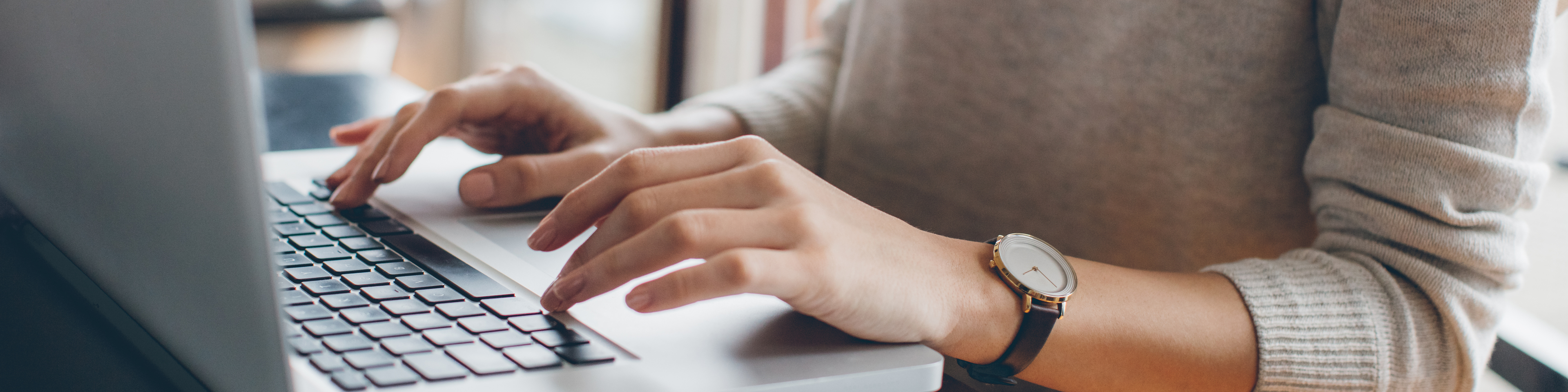 Woman with shoulder length hair and grey sweater sitting down using laptop, black and white face watch on left hand, Q3 2021, TAA NA US - Preparer