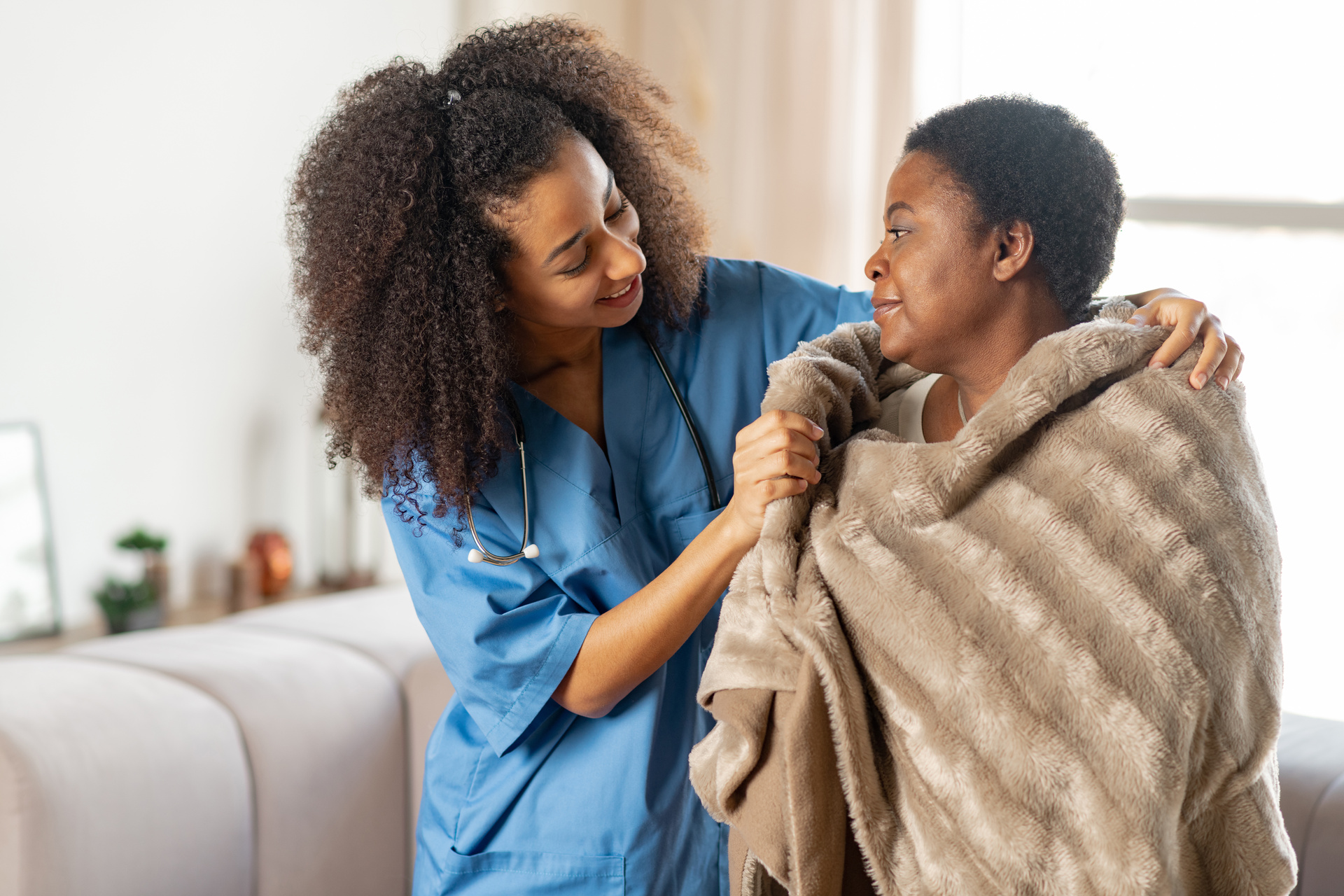 Certified nursing assistant helps to comfort patient by putting a blanket around their shoulders