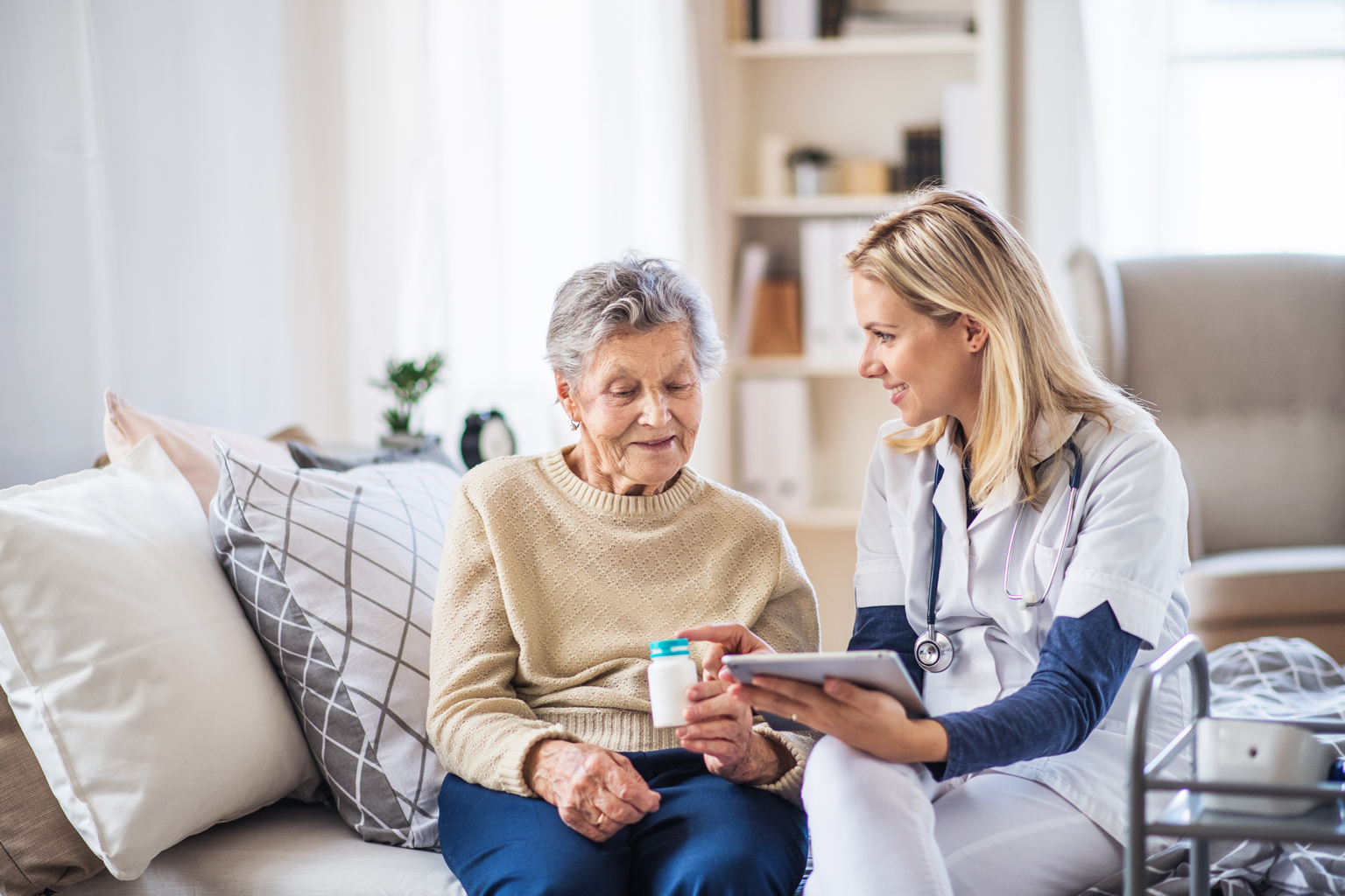 Home health nurse sitting with patient talking to her about the medication bottle patient is holding