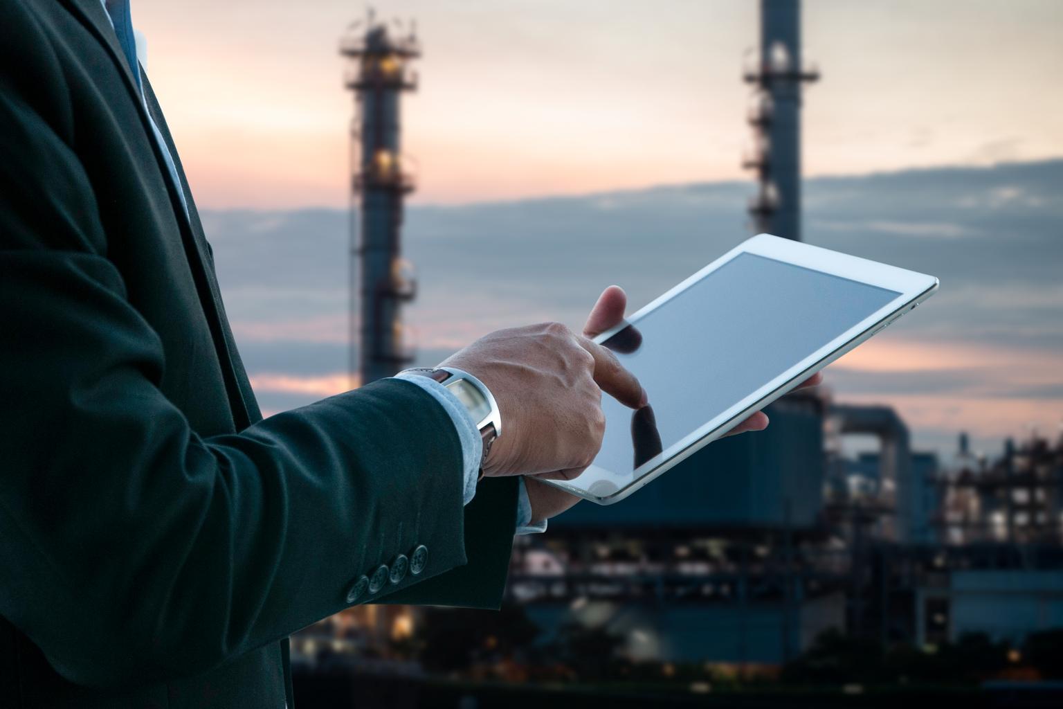 Business man working on media pad with oil and gas refinery background.