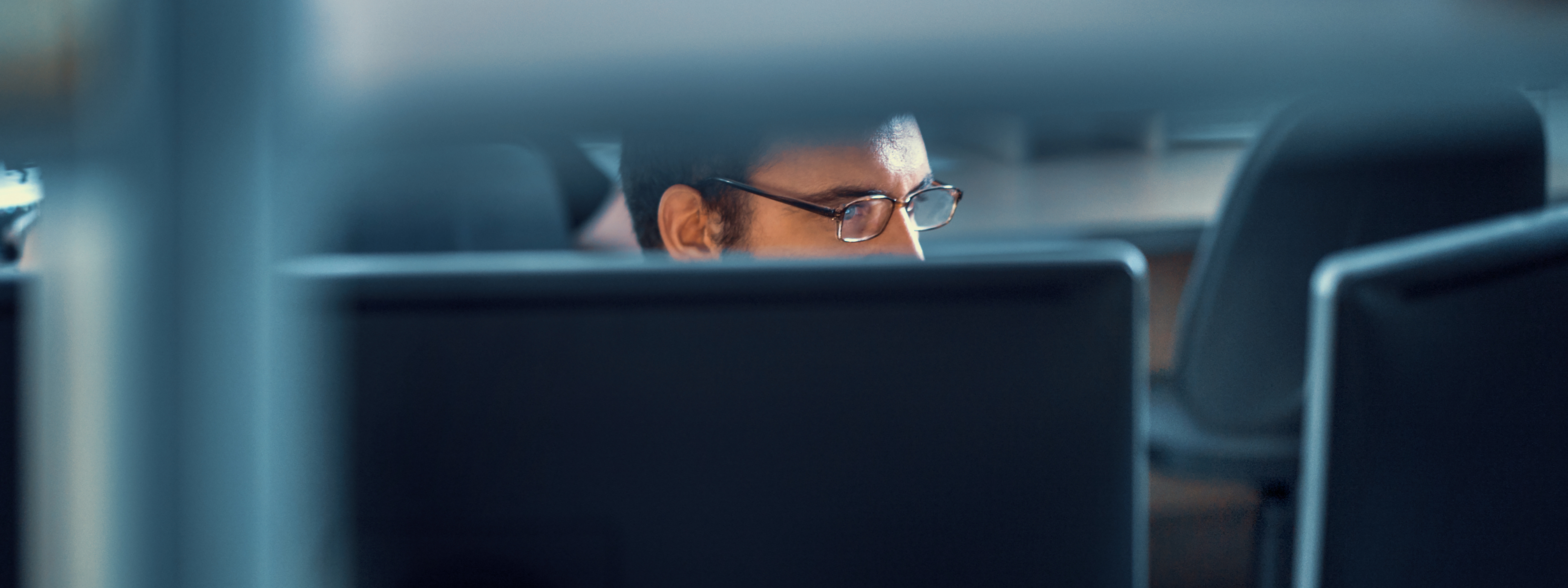 Closeup front view of deeply focus developer working on an application. He's sitting in front of dual display monitor, barely visible through office furniture