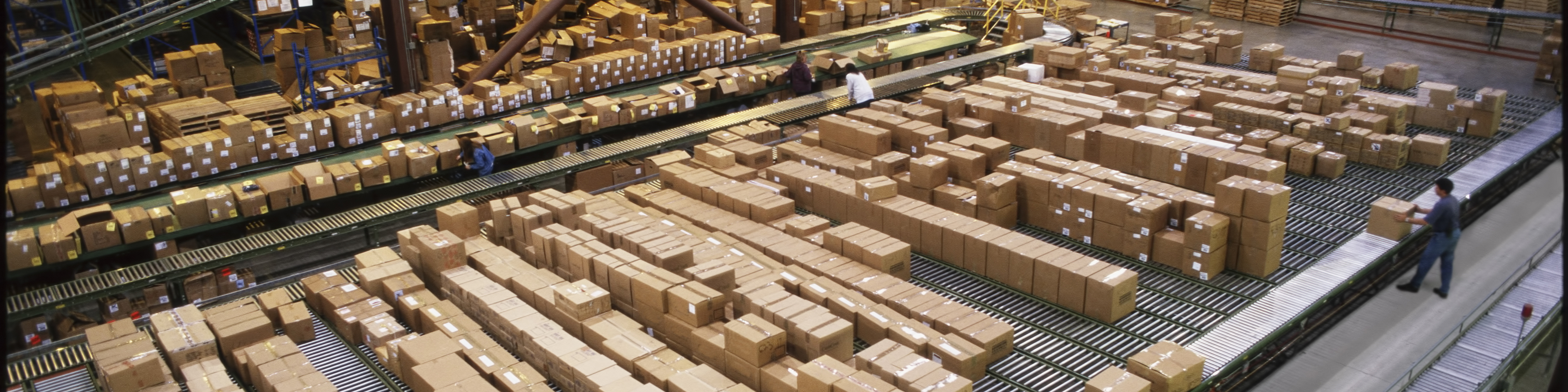 Overview of a large industrial distribution warehouse storing products in cardboard boxes on conveyor belts and racks.