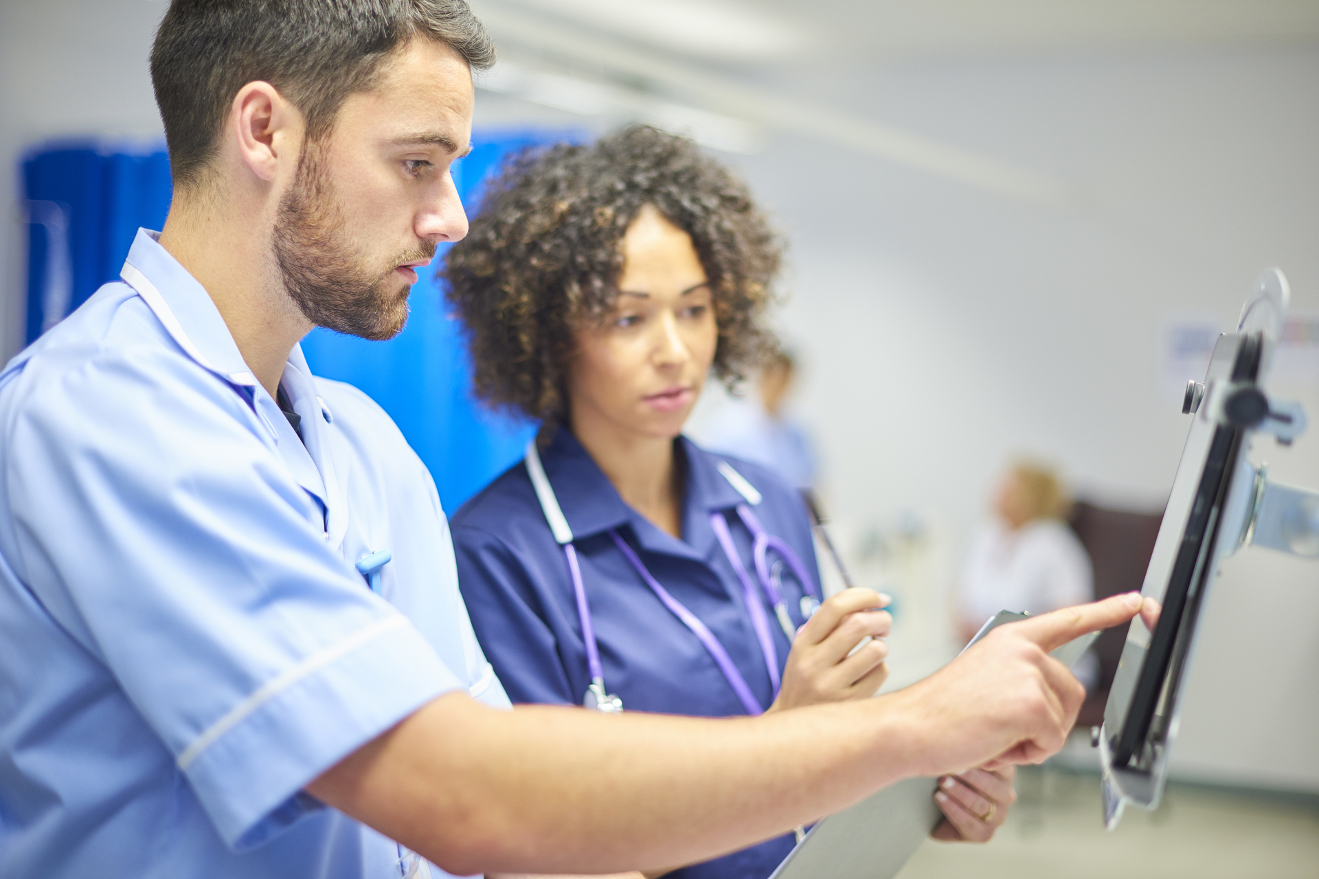 White male nurse checks the dosage on tablet supervised by female staff nurse.