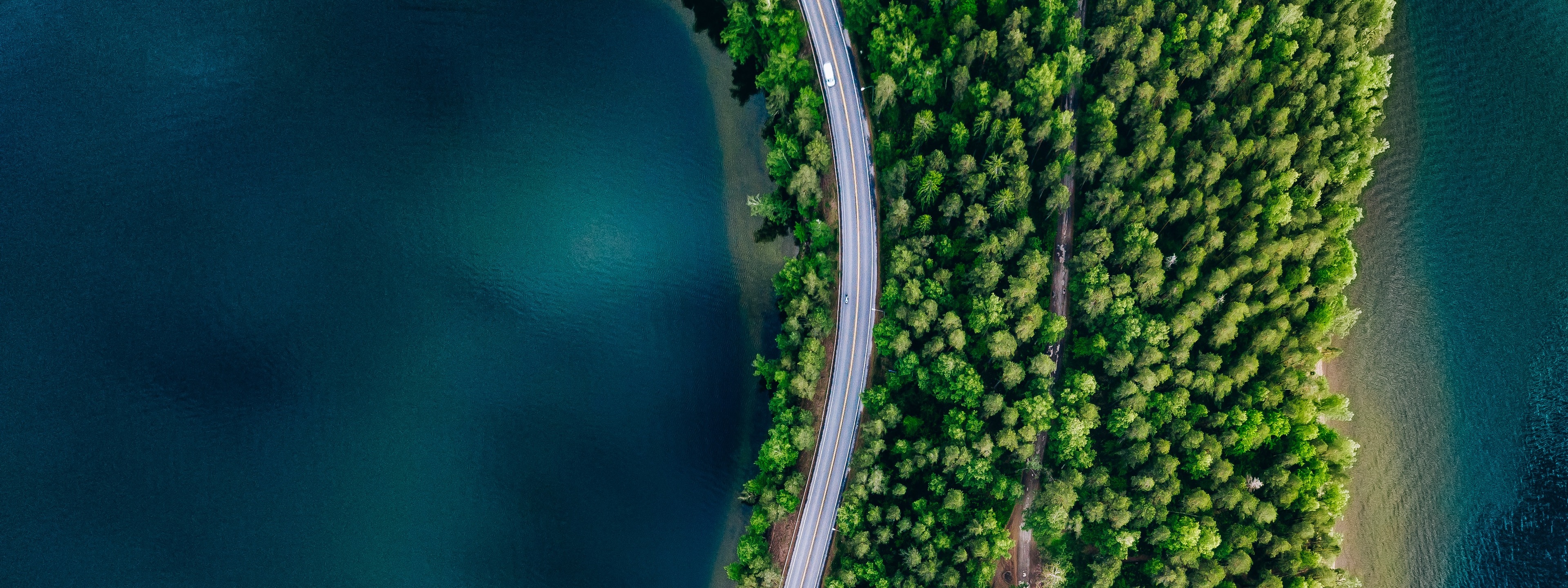 Aerial view of road between green forest and blue lake in Finland, 