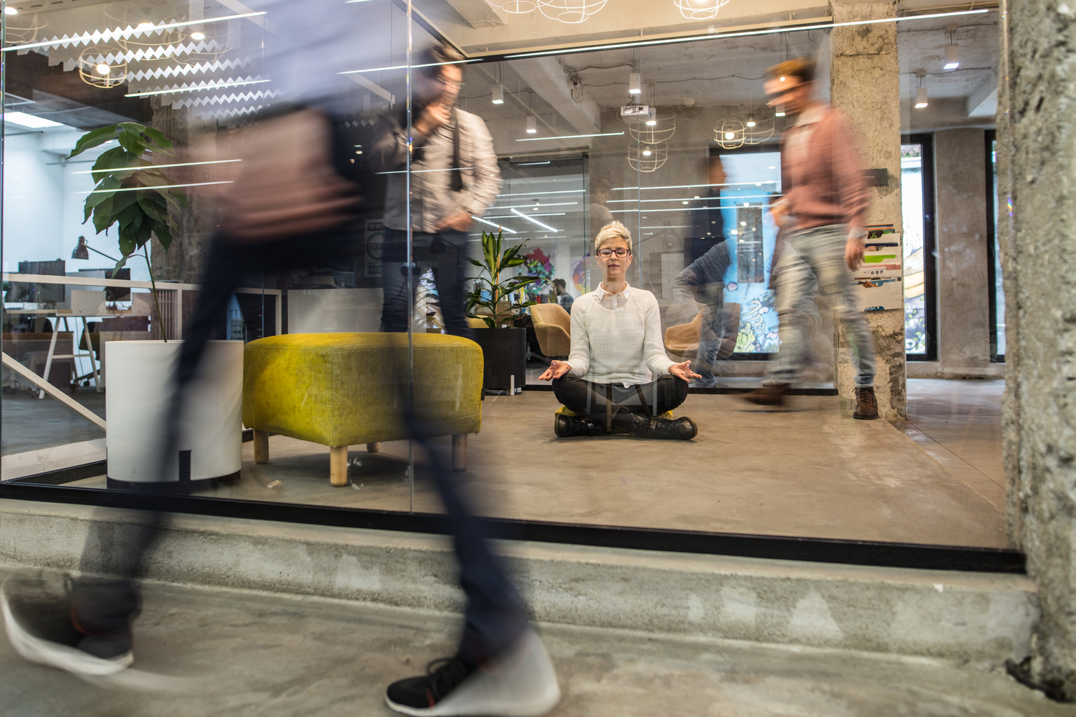 Young female entrepreneur meditating with eyes closed in busy office. 