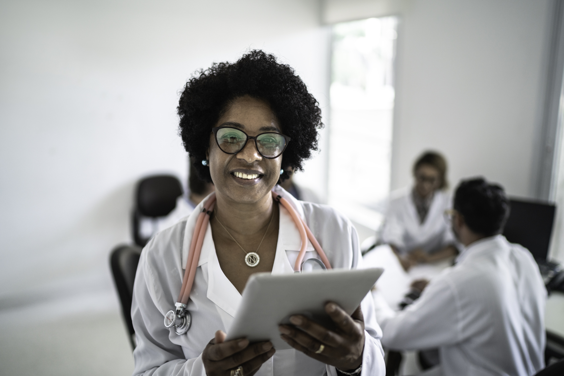 Portrait of mature female doctor using digital tablet with doctor's conference / meeting on background