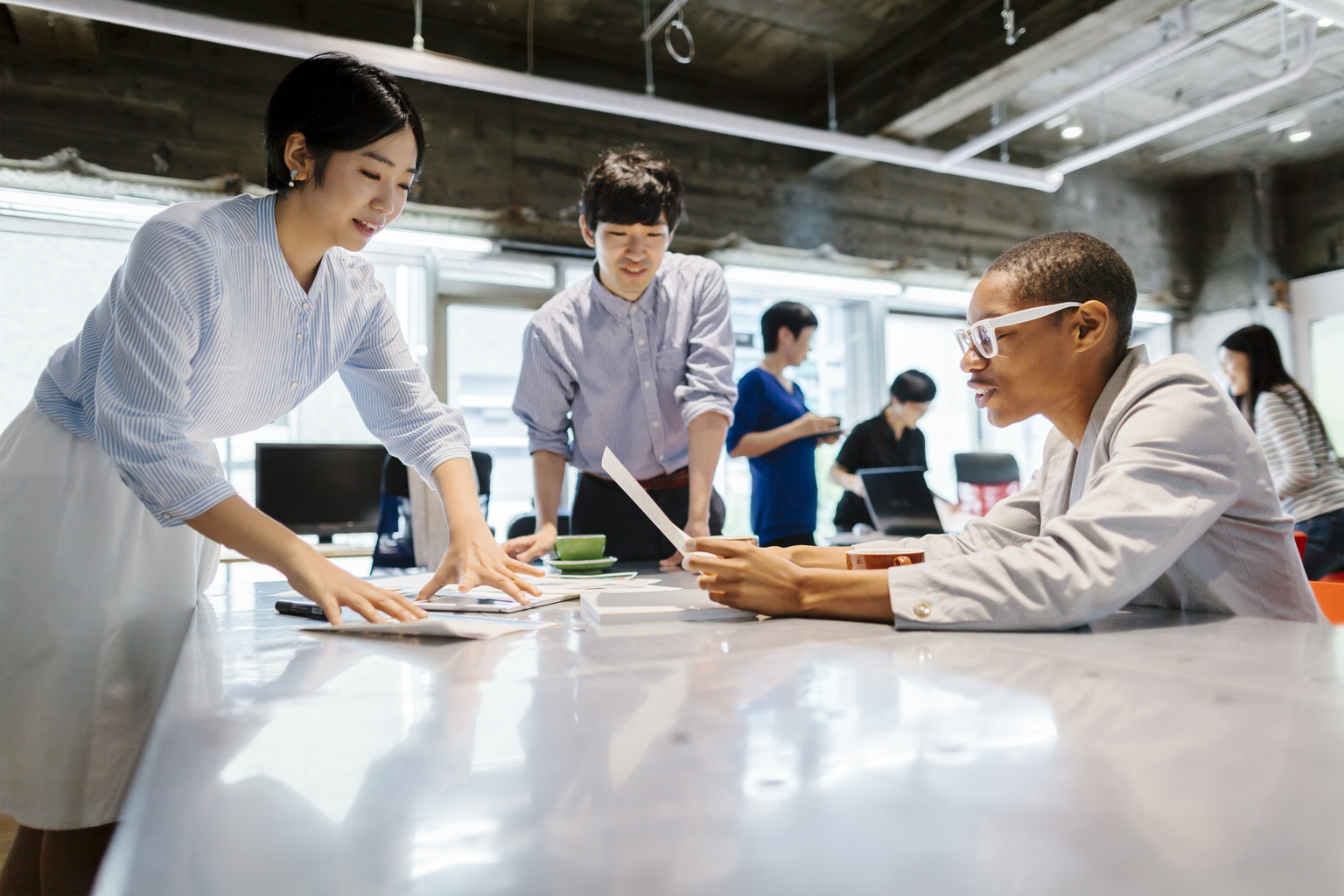 A group of multi-ethnic young business people are talking to each other in a modern working space in Tokyo.