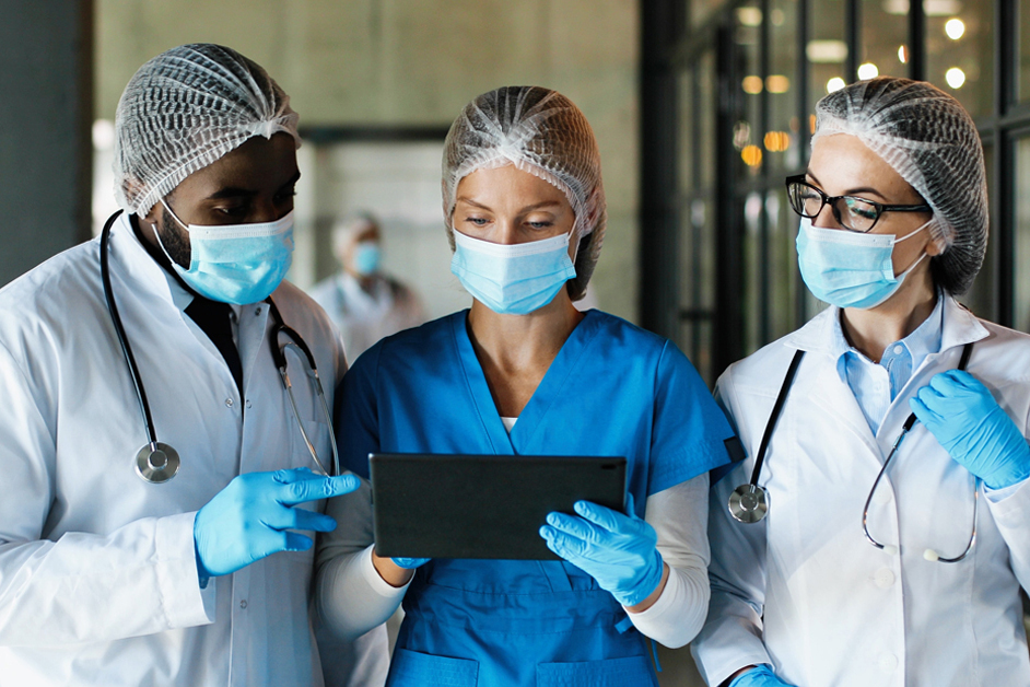 Doctors in medical masks and gloves, walking in hospital and talking using tablet