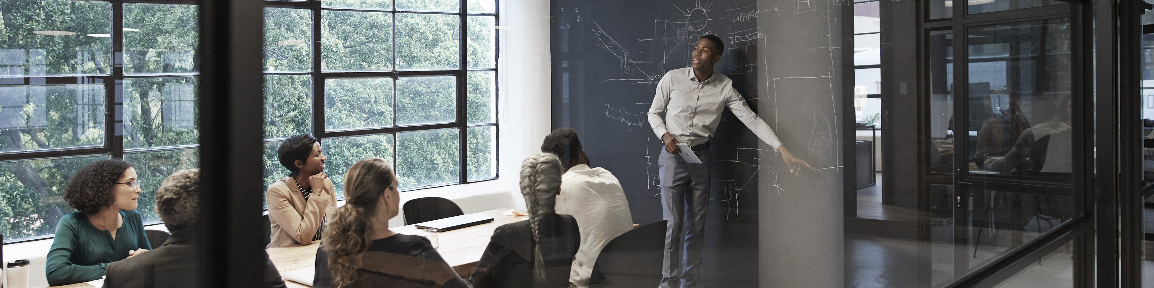 Businessman explaining while male and female colleagues sitting in conference room seen through glass wall at workplace.