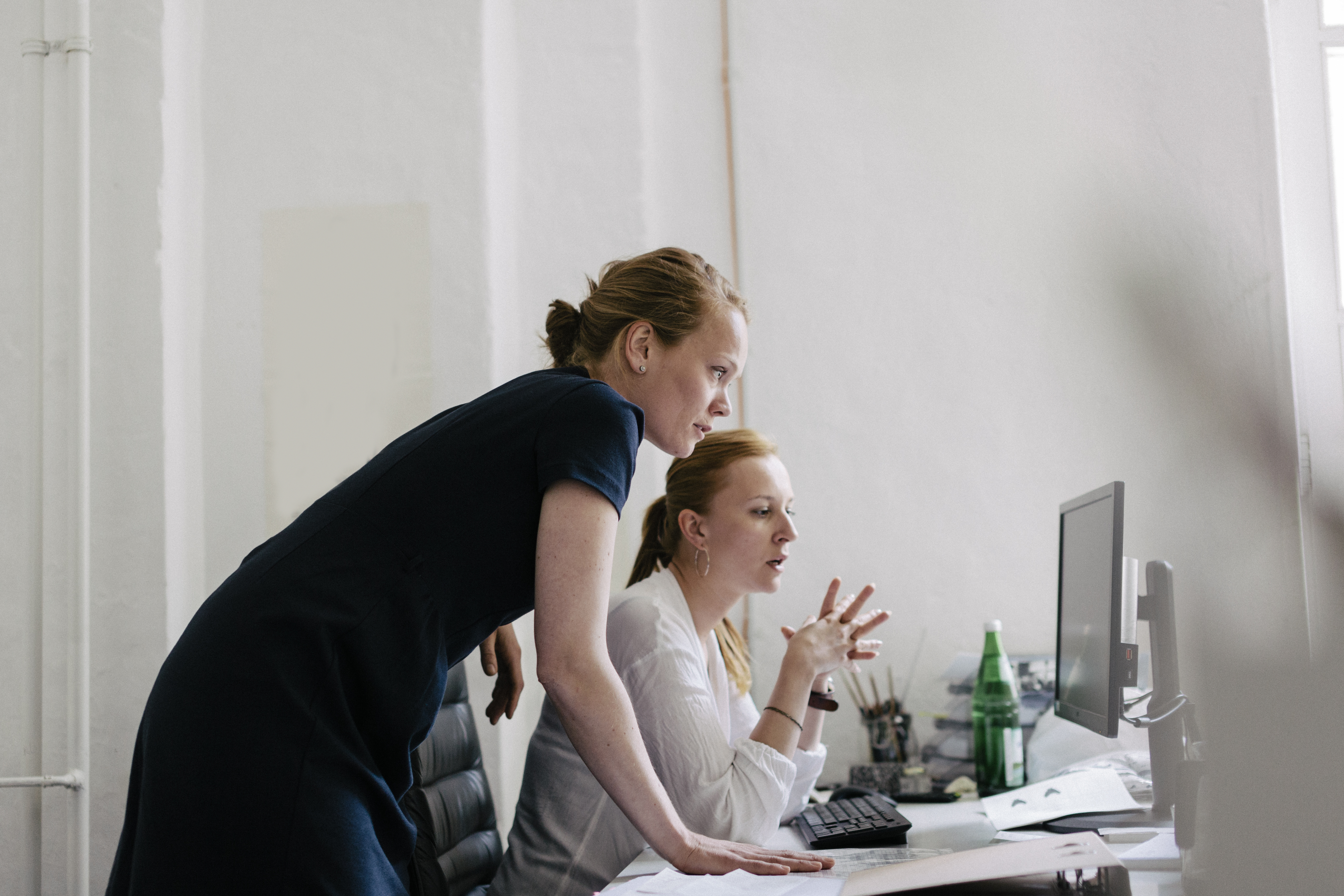 Two women working in an office. Both are leaning over a computer working as a team