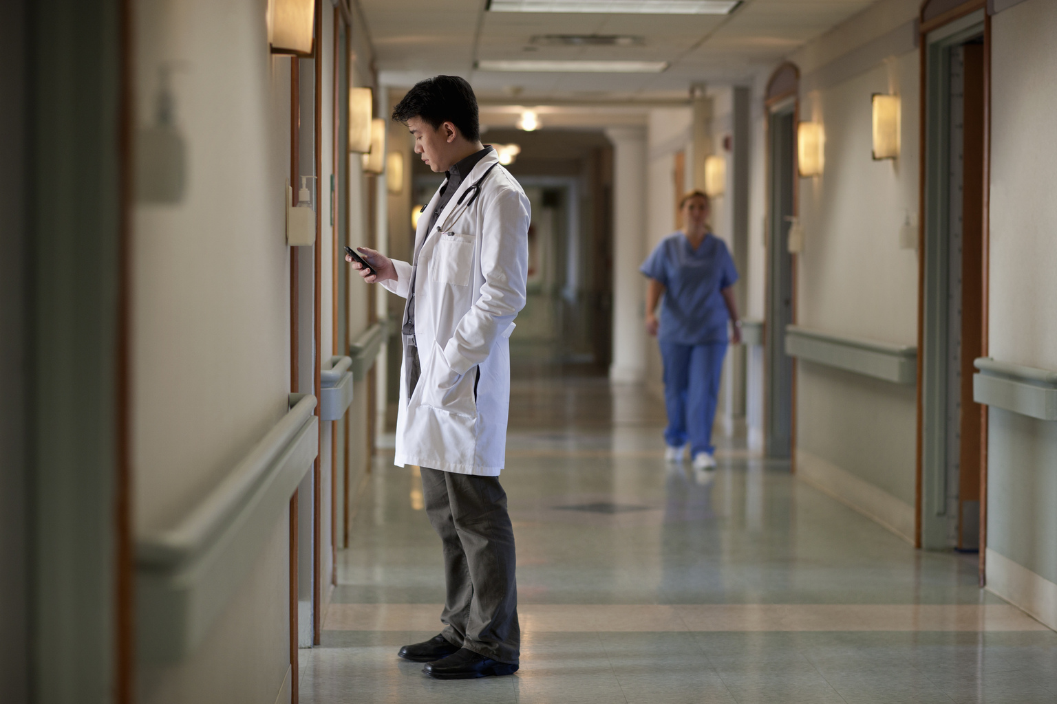 Asian male doctor in hospital corridor with phone.