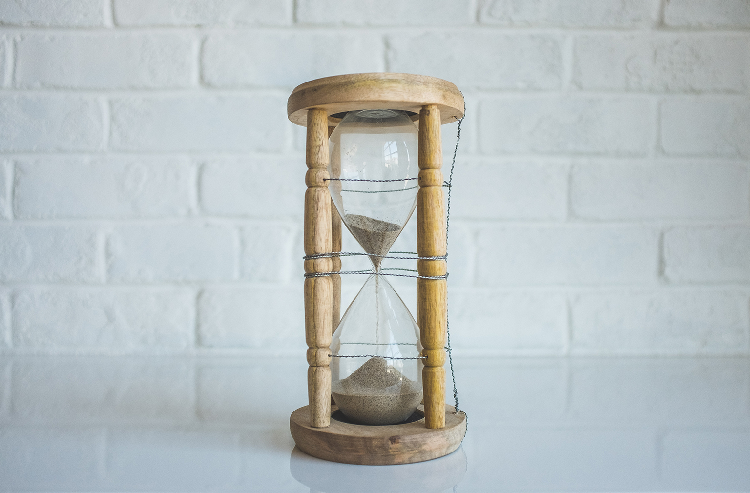 Hourglass sitting on white surface in front of white brick wall