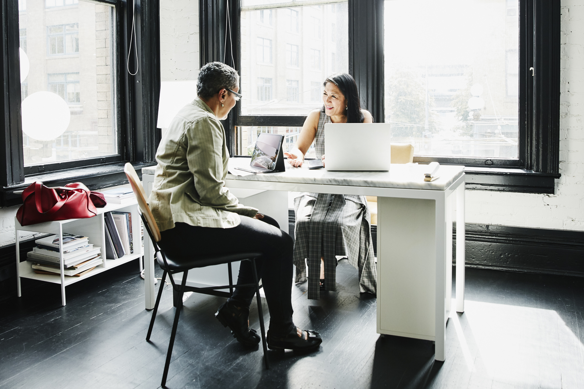 Smiling mature female business owner in discussion with financial advisor at desk in office