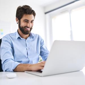 Smiling businessman with headphones sitting at a desk using a laptop