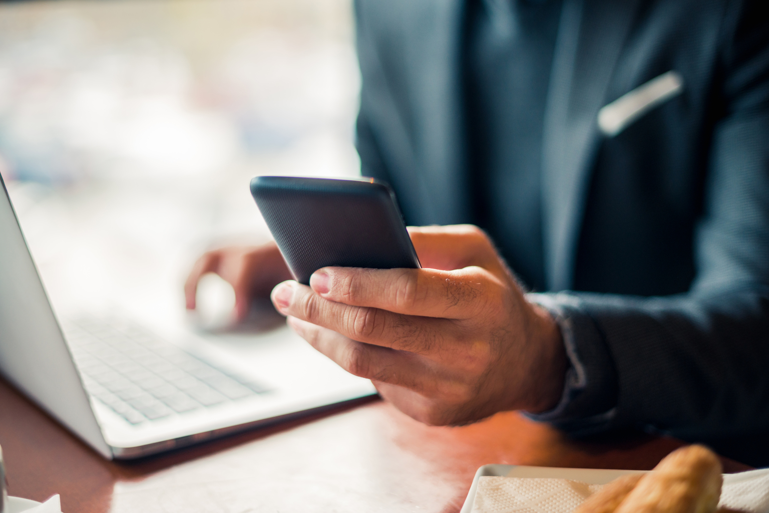 Man with Navy blue business suit holding his smart phone and using his laptop touchpad, Q3 2021, TAA NA US - Preparer