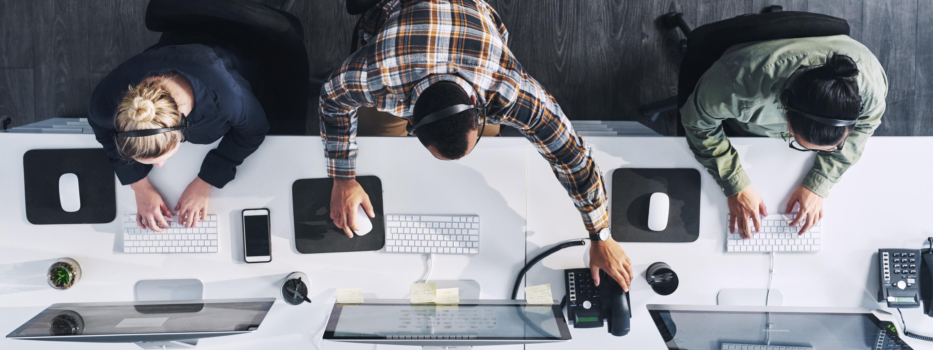 Above photography image of three, 3 employees, plaid shirt, green shier, a navy shirt, working at white desk on Imac, Q3 2021, TAA NA US - Preparer