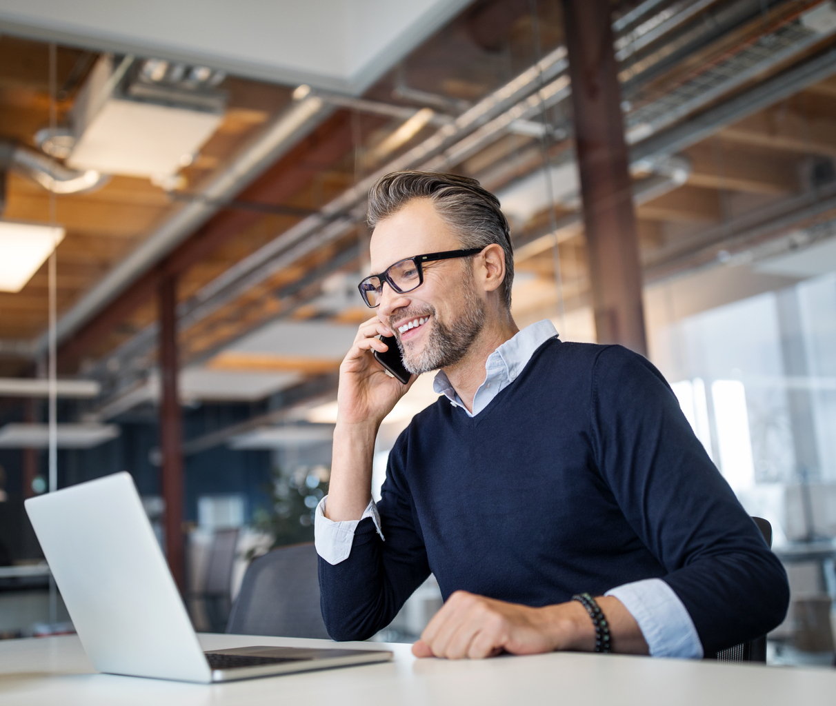 Man with black glasses, blue collared shirt, black bead bracelet and navy sweatshirt sitting down and smiling on the phone, Q3 2021, TAA NA US - Preparer