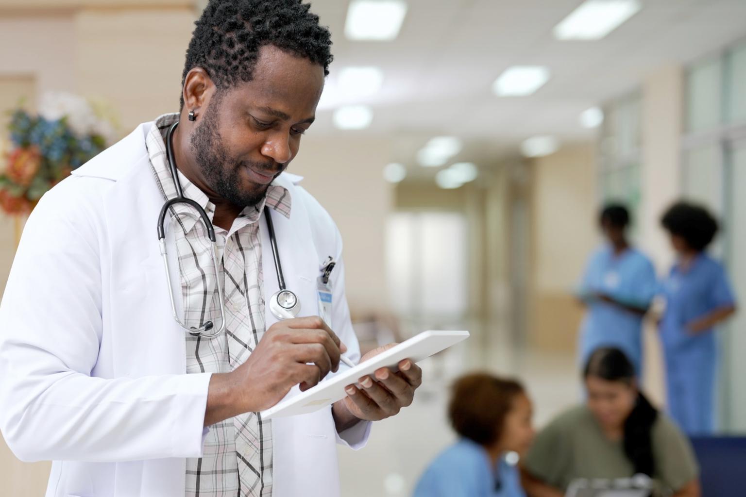 Black doctor making notes on tablet in hospital