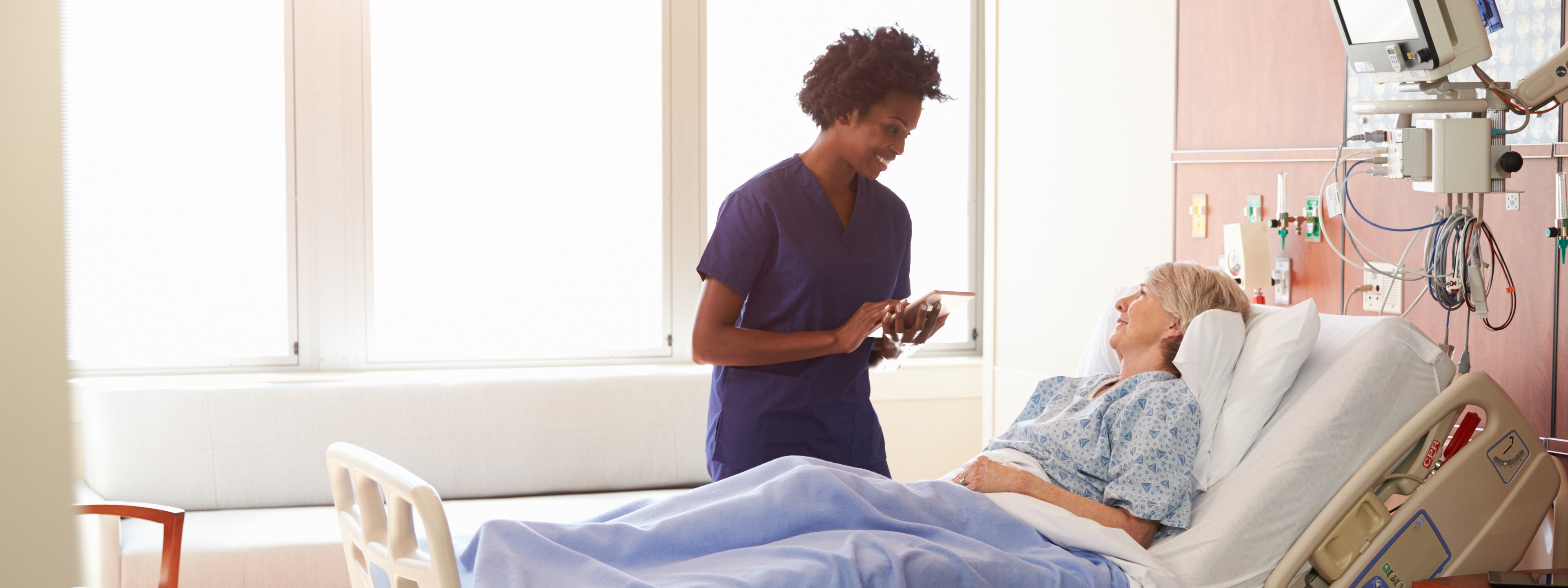 Hospital Nurse With Digital Tablet Talks To Senior Patient