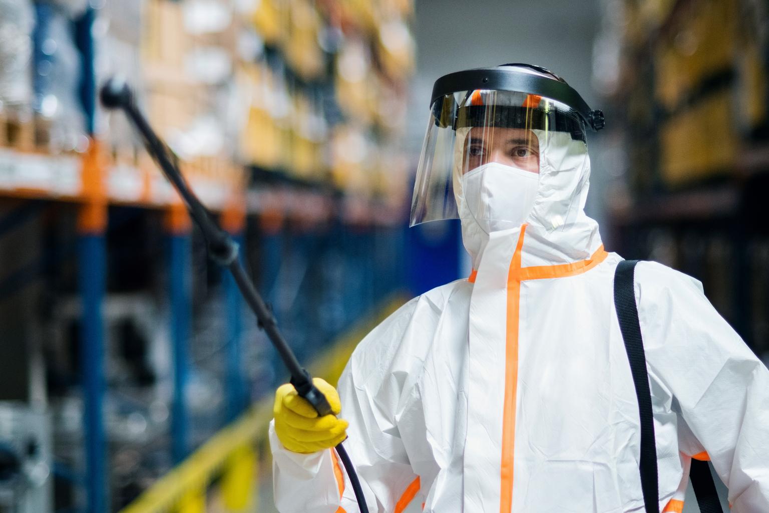 Man worker with protective mask and suit disinfecting industrial factory with spray gun.