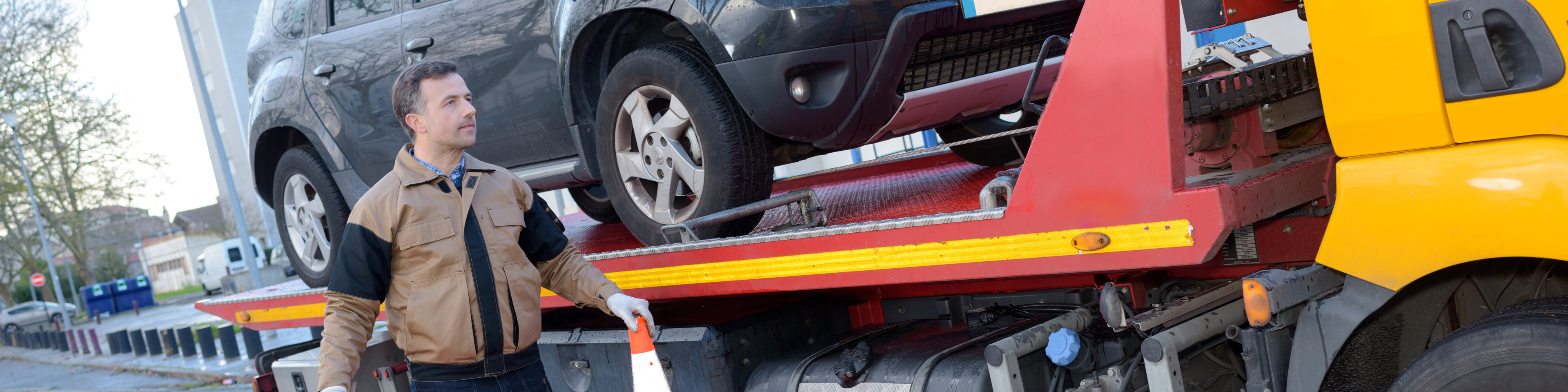 Man standing in front of a flat bed truck with an SUV on it.