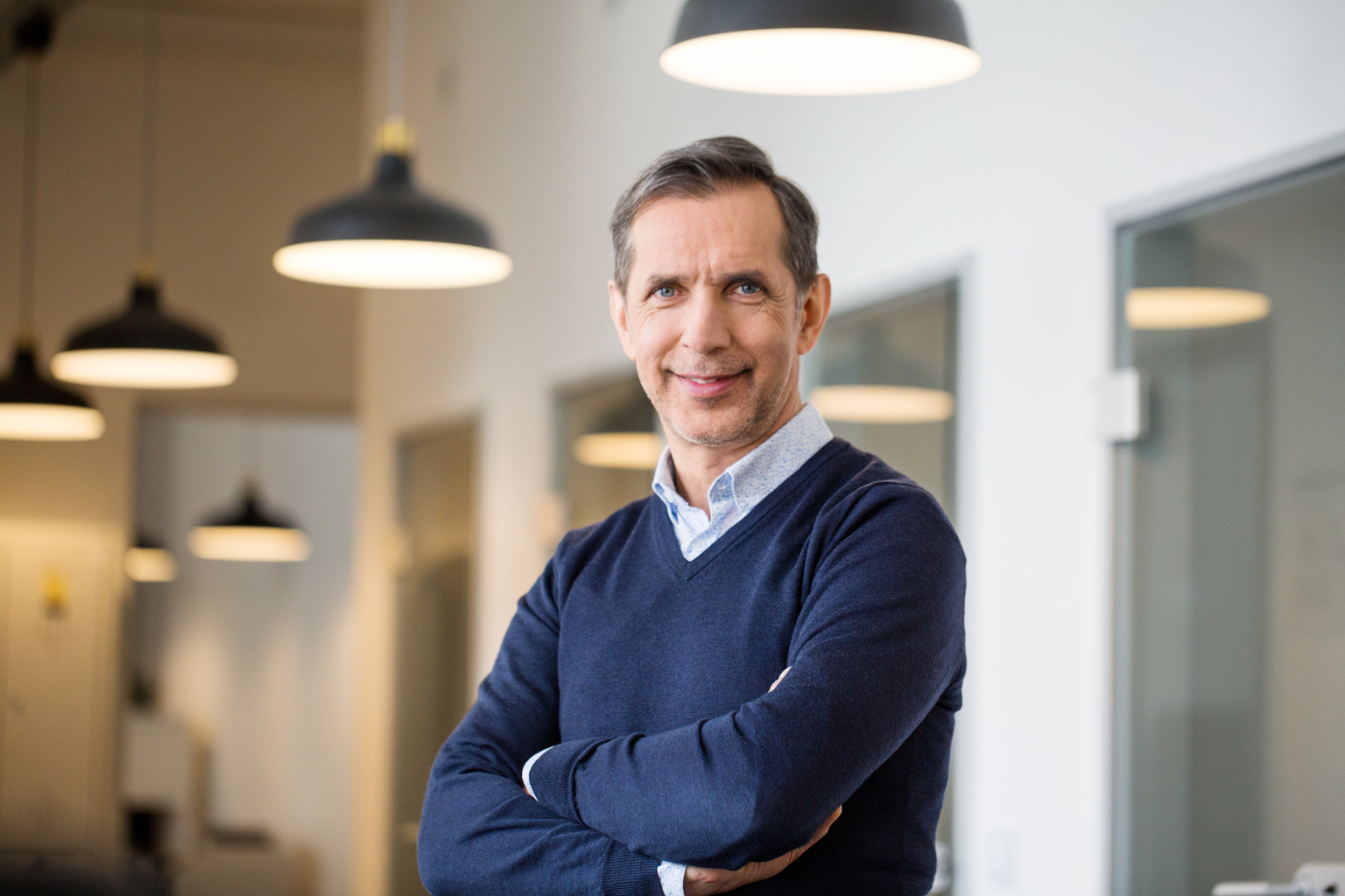 Portrait of a happy mature business professional standing with his arms crossed in modern office. Smiling businessman at his workplace.