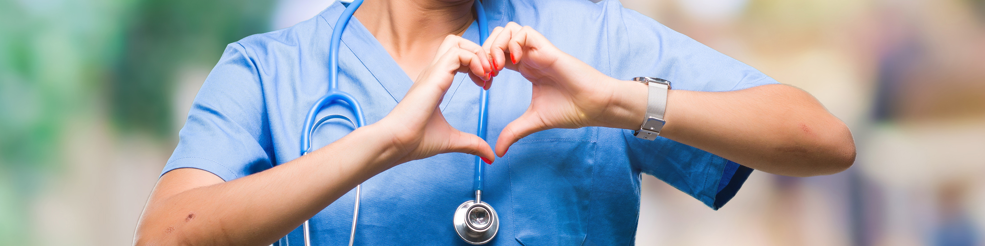 Woman in hospital scrubs smiling and showing heart symbol with her hands