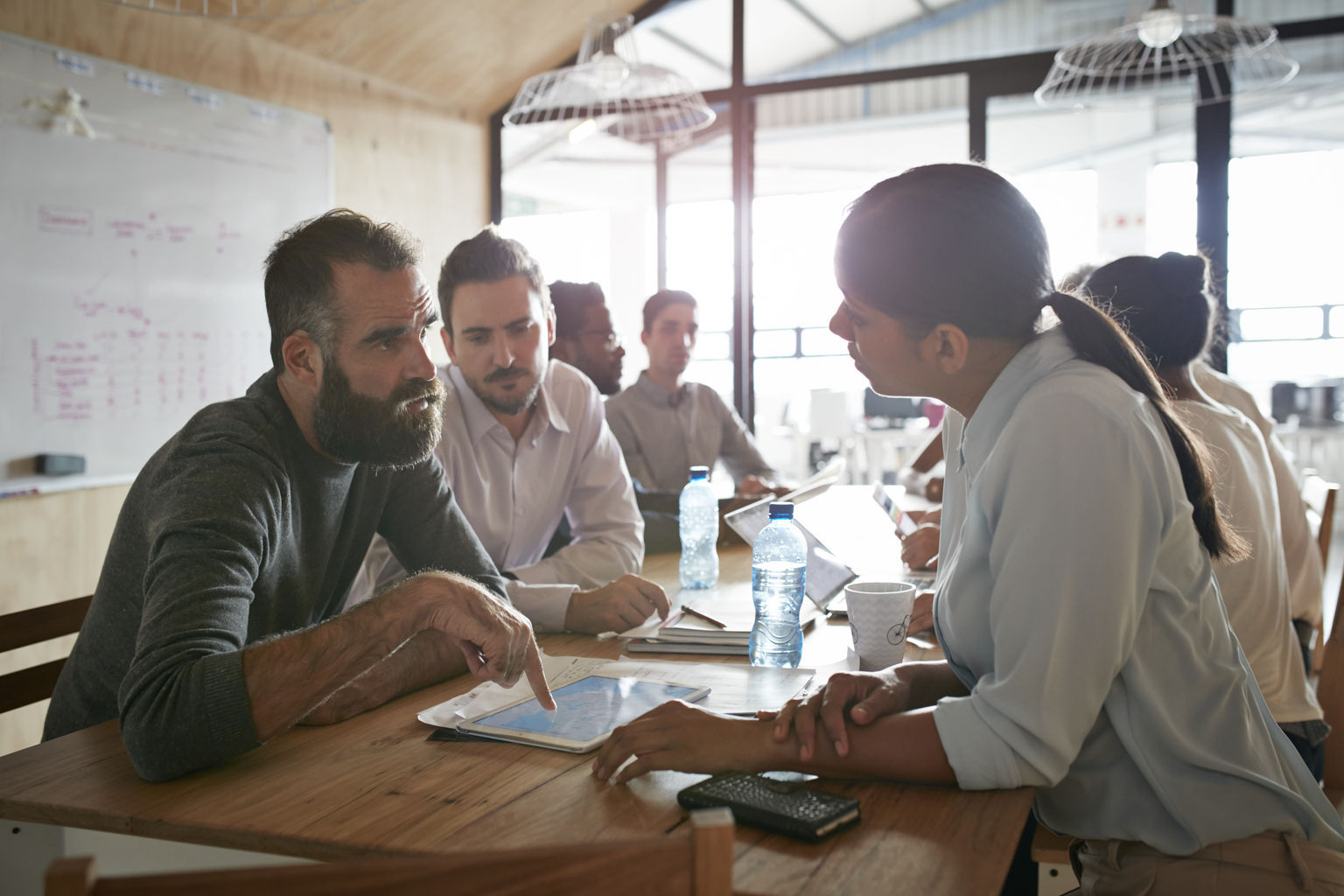 Businesspeople having meeting at big creative agency, man explaining to coworkers using tablet