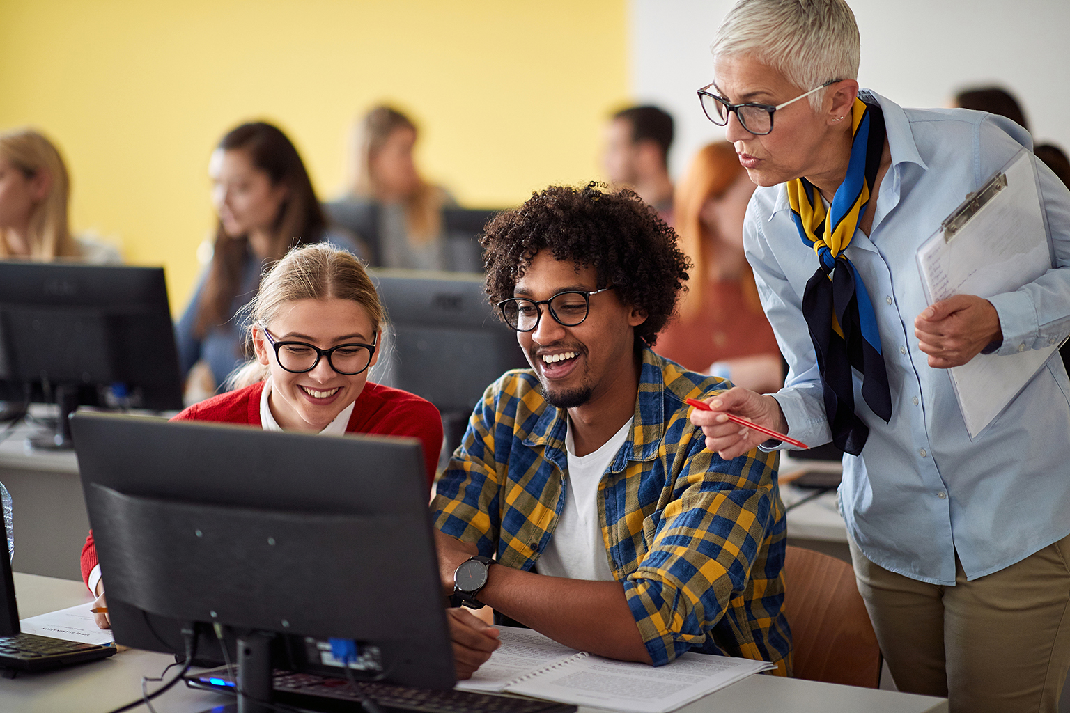 Educator overlooking two students at a computer