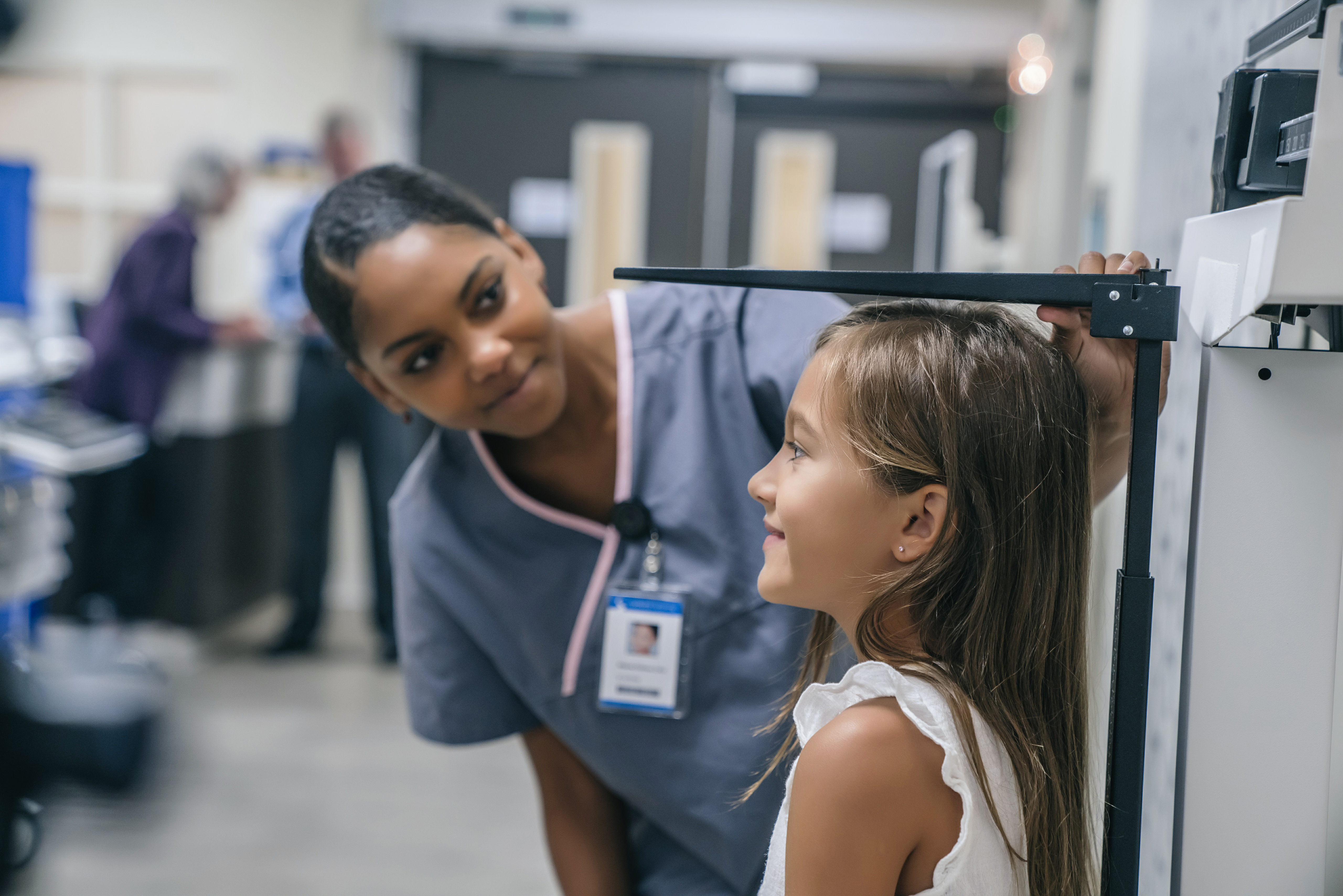 African female nurse checks the height of young girl.