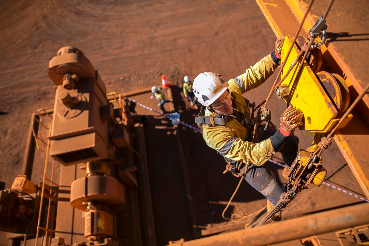 Rope access maintenance worker wearing safety harness hard hat working at height descending on rope performing inspecting lifting chain block on beam clamp trolley prior to use construction site Perth