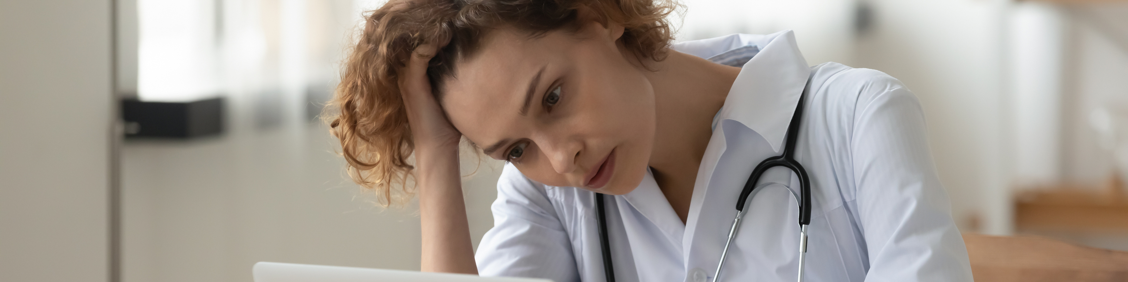Stressed young female doctor looking at laptop worried