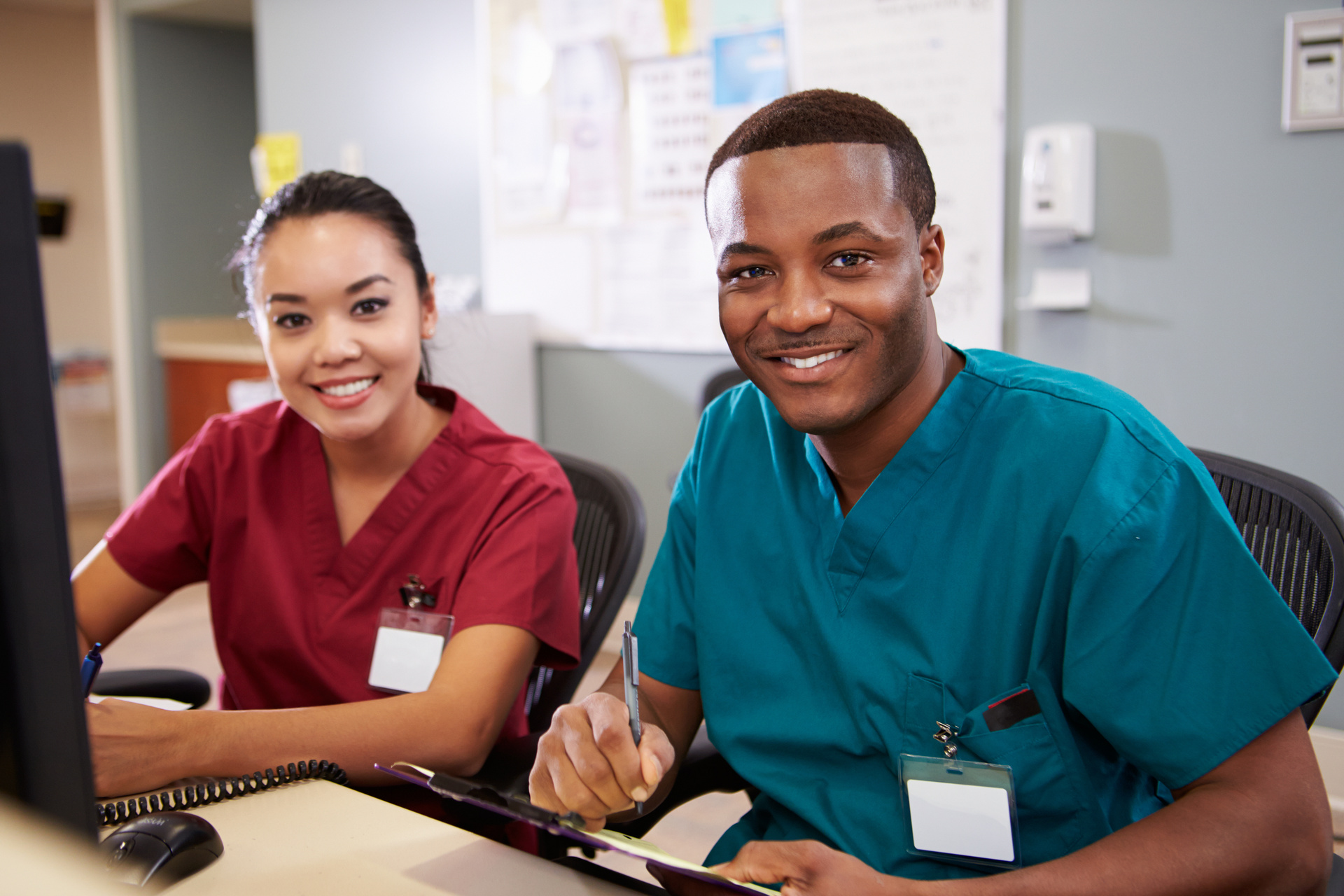 Two smiling medical professionals sitting at a desk with a computer within a medical setting