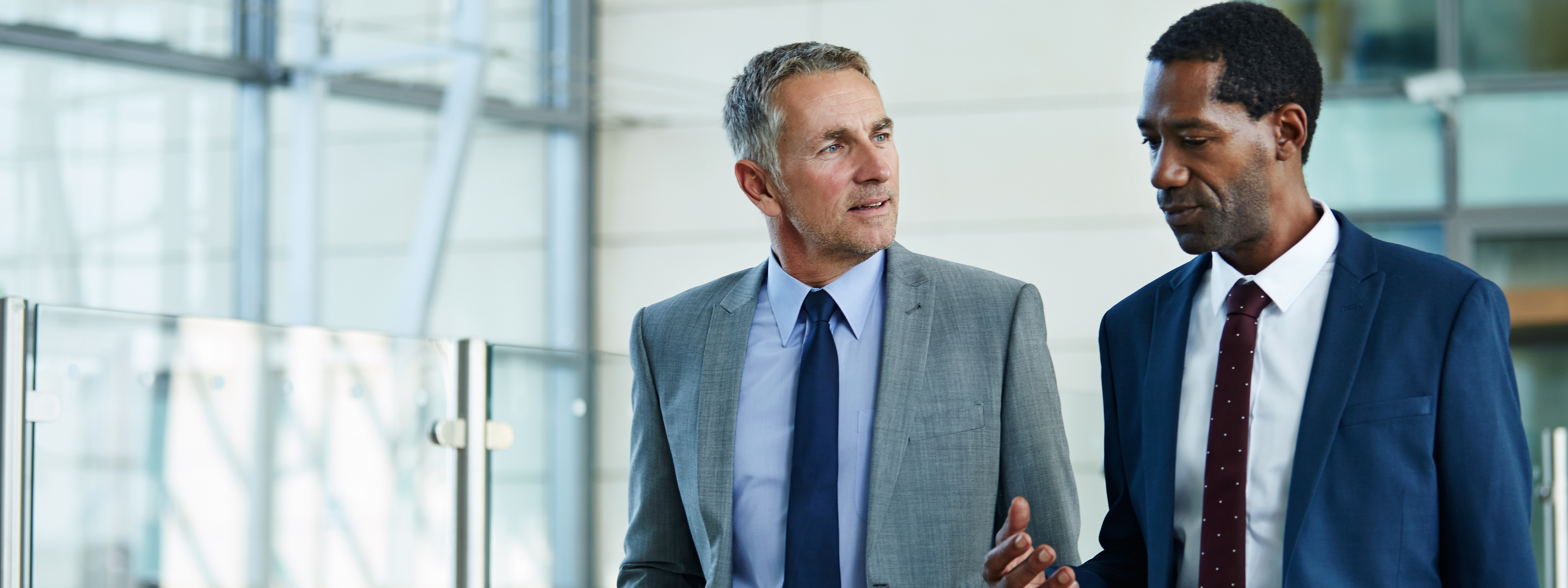 Shot of two businessmen walking and talking together in the lobby of an office building