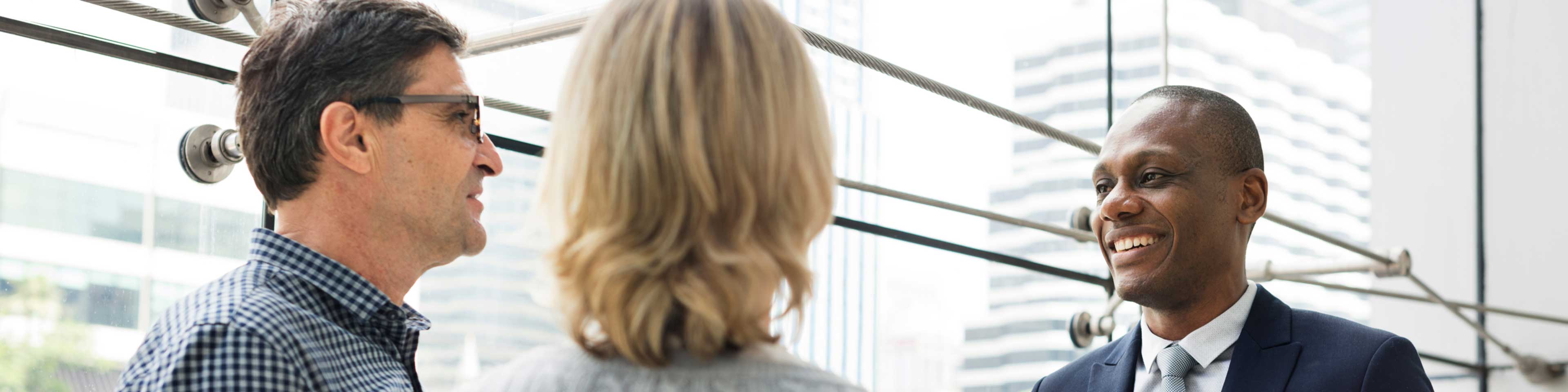 Three people standing by a large window having a discussion