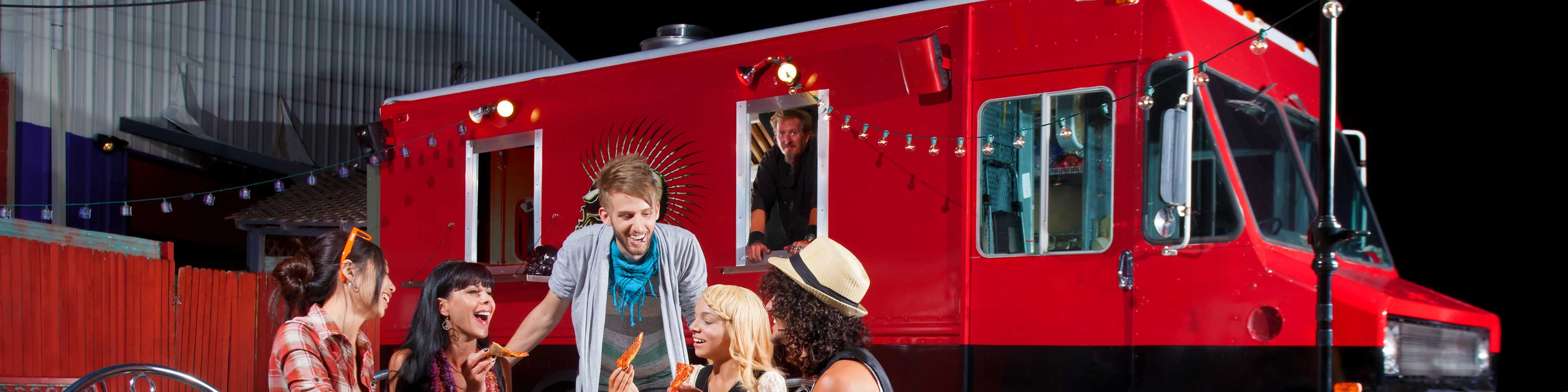 5 people eating  outside of a red food truck