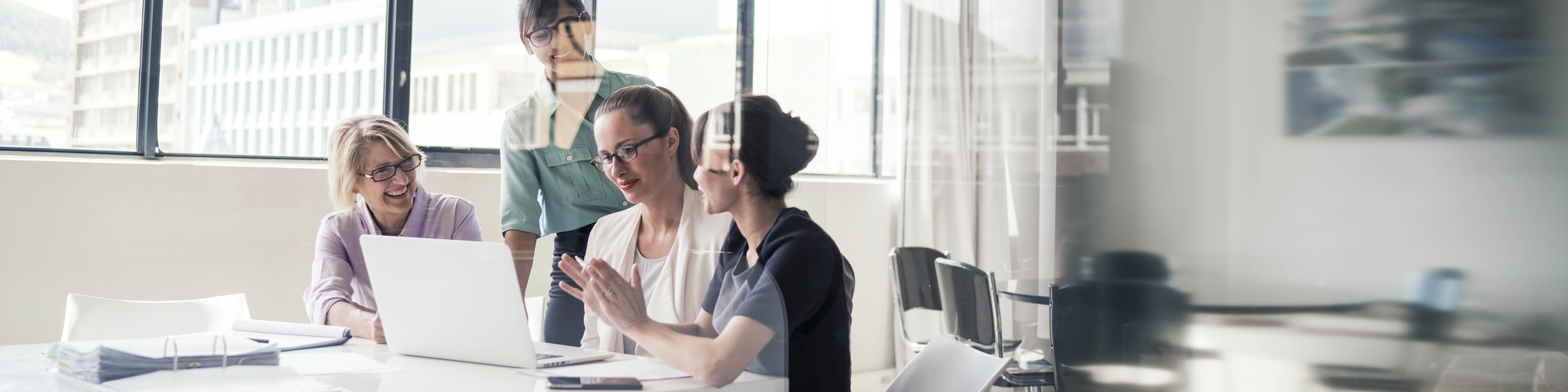 A photo of multi-ethnic businesswomen discussing over laptop in office. Female professionals are in formals. Executives are in meeting at brightly lit workplace.