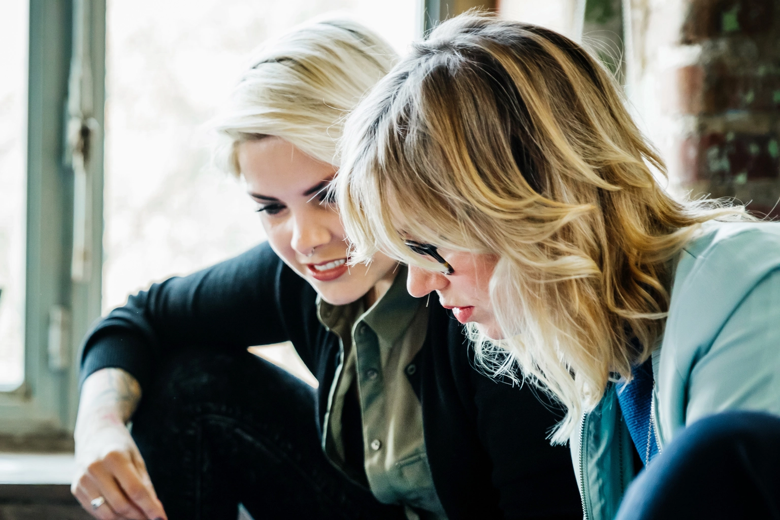 Professional women sitting casually on the floor discussing data on sheets and devices