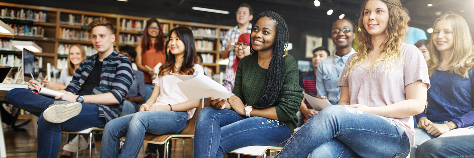 Students sitting in rows of seats in library, listening to a lecturer