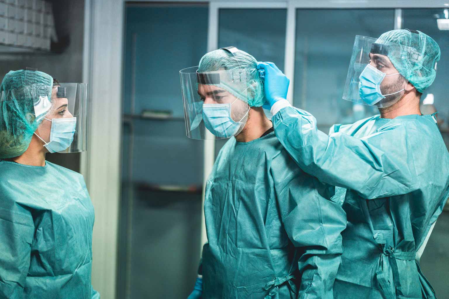 Three healthcare professionals getting in personal protective equipment