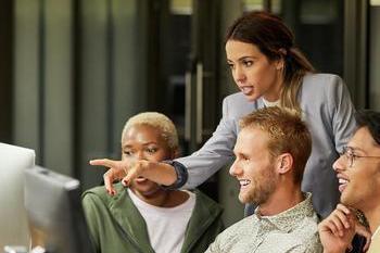 Businesswoman pointing while discussing with coworkers over computer monitor