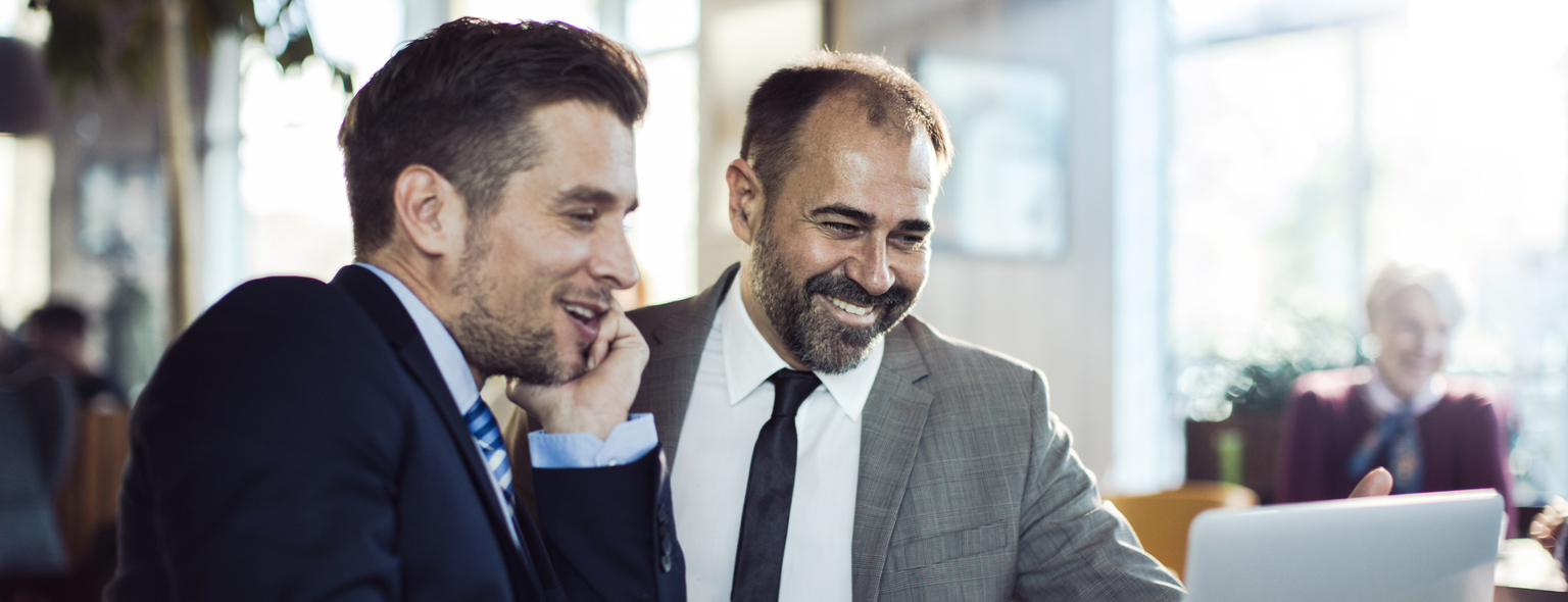 Colleagues smiling with a cup of coffee and discussing over a Laptop